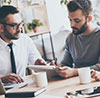 Three office workers collaborating with coffee and a tablet.