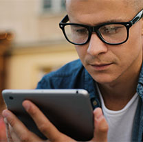 Person wearing glasses looking at tablet held in their hand.
