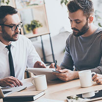 Three office workers collaborating with coffee and a tablet.